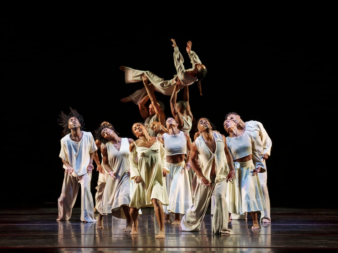 A group of dancers on a stage life one dancer above their heads