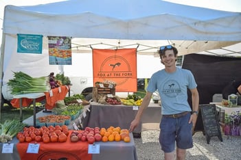 a man stands beside produce at a farmers market