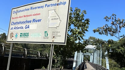 Signage advertising the BacteriAlert program and its participating partners in front of a bridge and blue sky.