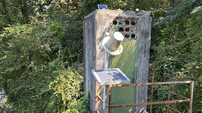 A river gage on the Chattahoochee River. A rectangular, gray metal box with small tubes surrounded by trees.