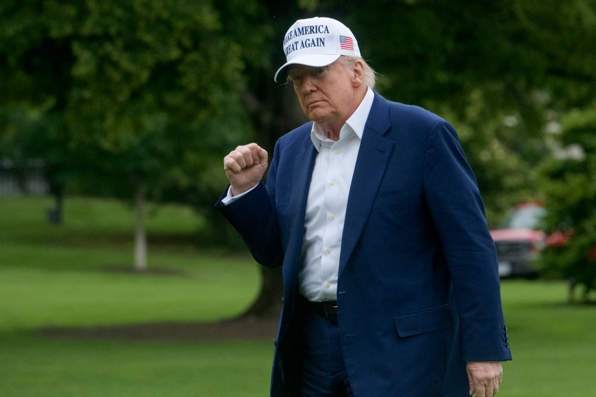 President Donald Trump wears a white Make America Great Again cap and holds up a fist on the South Lawn of the White House.