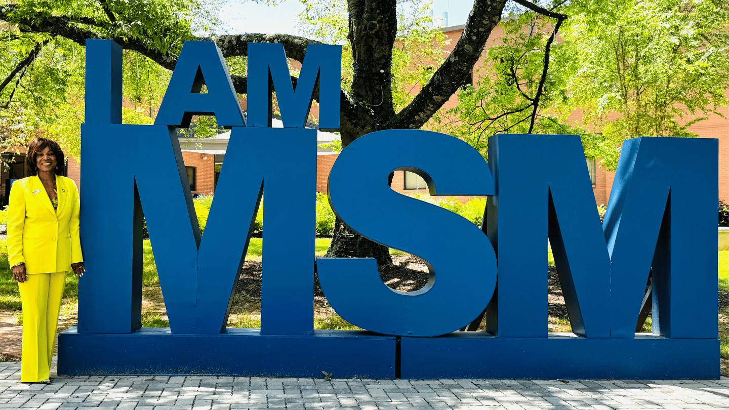 Valerie Montgomery Rice stands next to a blue statue that says I Am MSM.