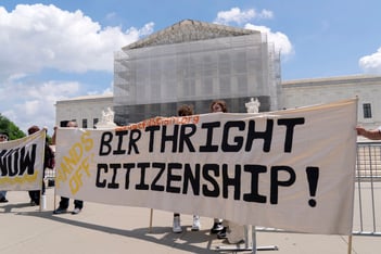 Demonstrators outside of the Supreme Court rally in support for birthright citizenship, holding a large white banner.