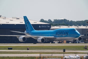 A blue Korean air plane taxis at an airport in front of the Delta logo