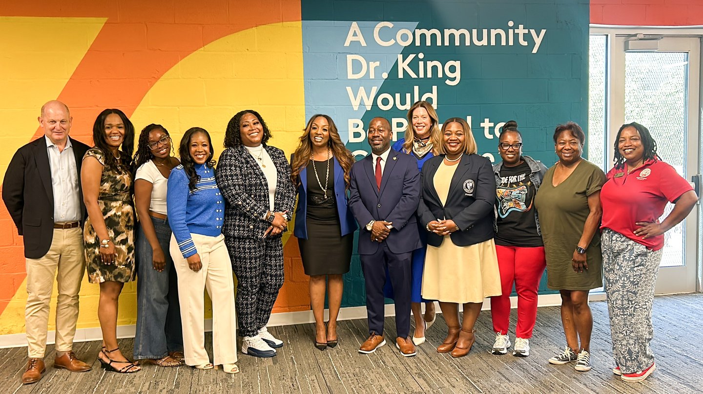 A group of well dressed people pose in front of a colorful wall after receiving a check to support schools in the area.