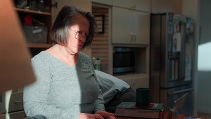 A woman looks at a computer on a kitchen counter