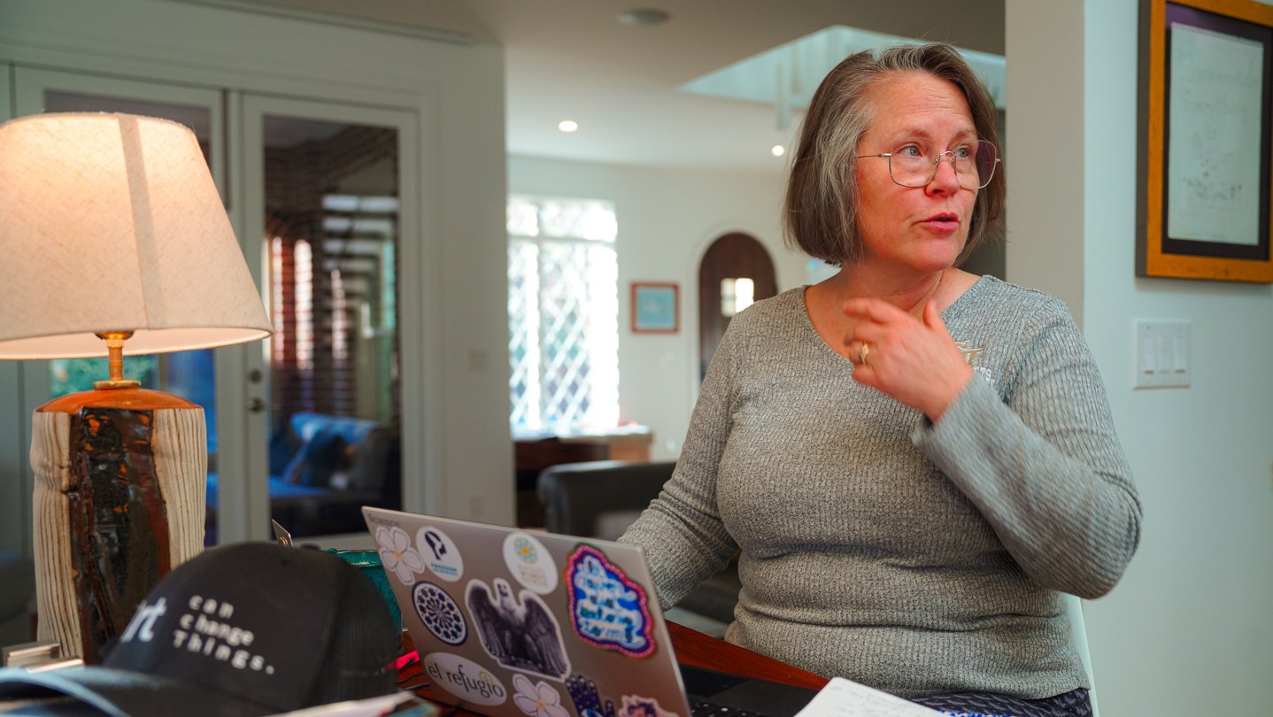 A woman stands in front of a laptop on a kitchen counter and looks off to the side