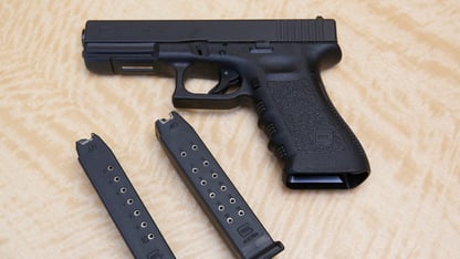 A hand gun, a 10 shot magazine, and a 15 shot magazine on a table.