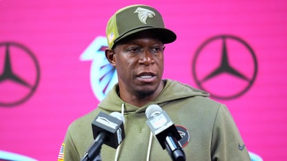 Atlanta Falcons head coach Raheem Morris talks into several microphones against a pink Mercedes Benz backdrop.