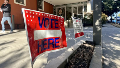 A read voting sign with a white arrow pointing to a polling location