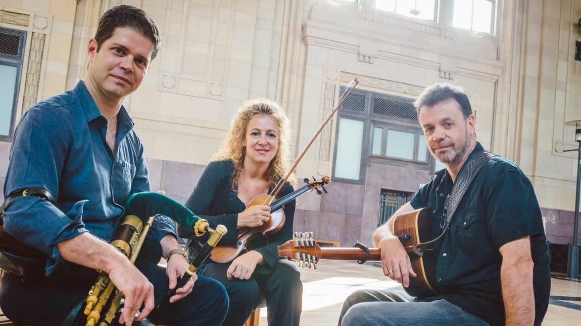 Three musicians seated indoors with instruments after a performance.