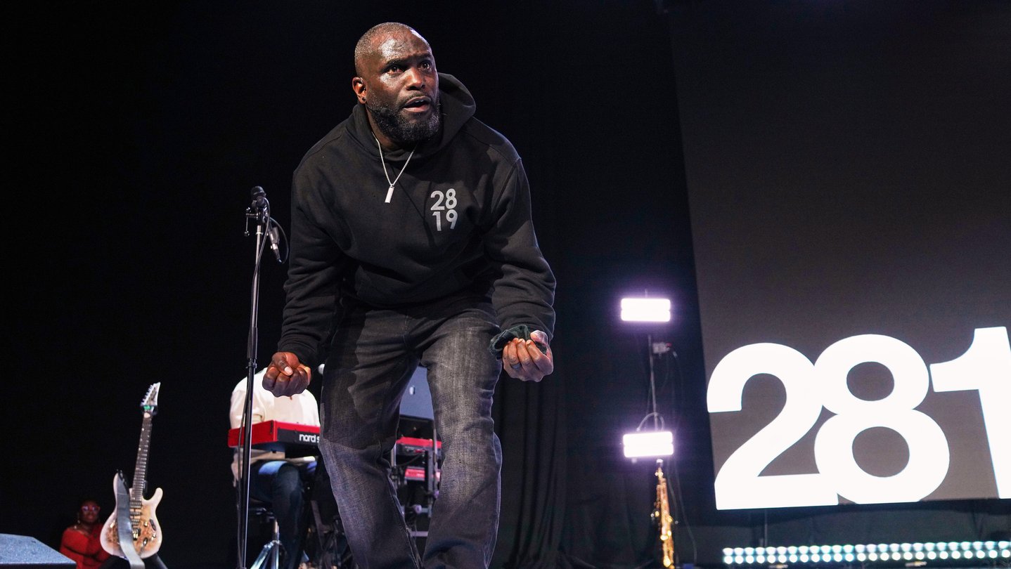 Pastor Philip Anthony Mitchel crouches down on a stage.