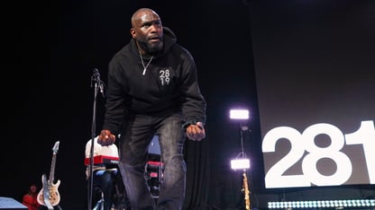 Pastor Philip Anthony Mitchel crouches down on a stage.