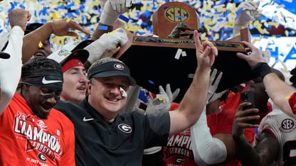 Georgia football players and coach Kirby Smart raise their hands up in celebration at a football game