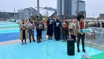 A group of people holding up a booklet on a bridge.