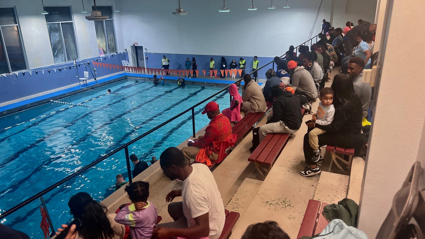 People sit on bleachers above a swimming pool