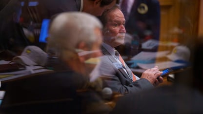 Behind a glass, two state senators sit in the Senate chamber.