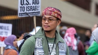 Yaacub Vijandre, wearing a bandana around his head and a keffiyeh on his shoulders. He is standing in a crowd of protesters