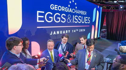 Reporters crowd around Chris Clark in front of a blue background at the Georgia Chamber Eggs and Issues event