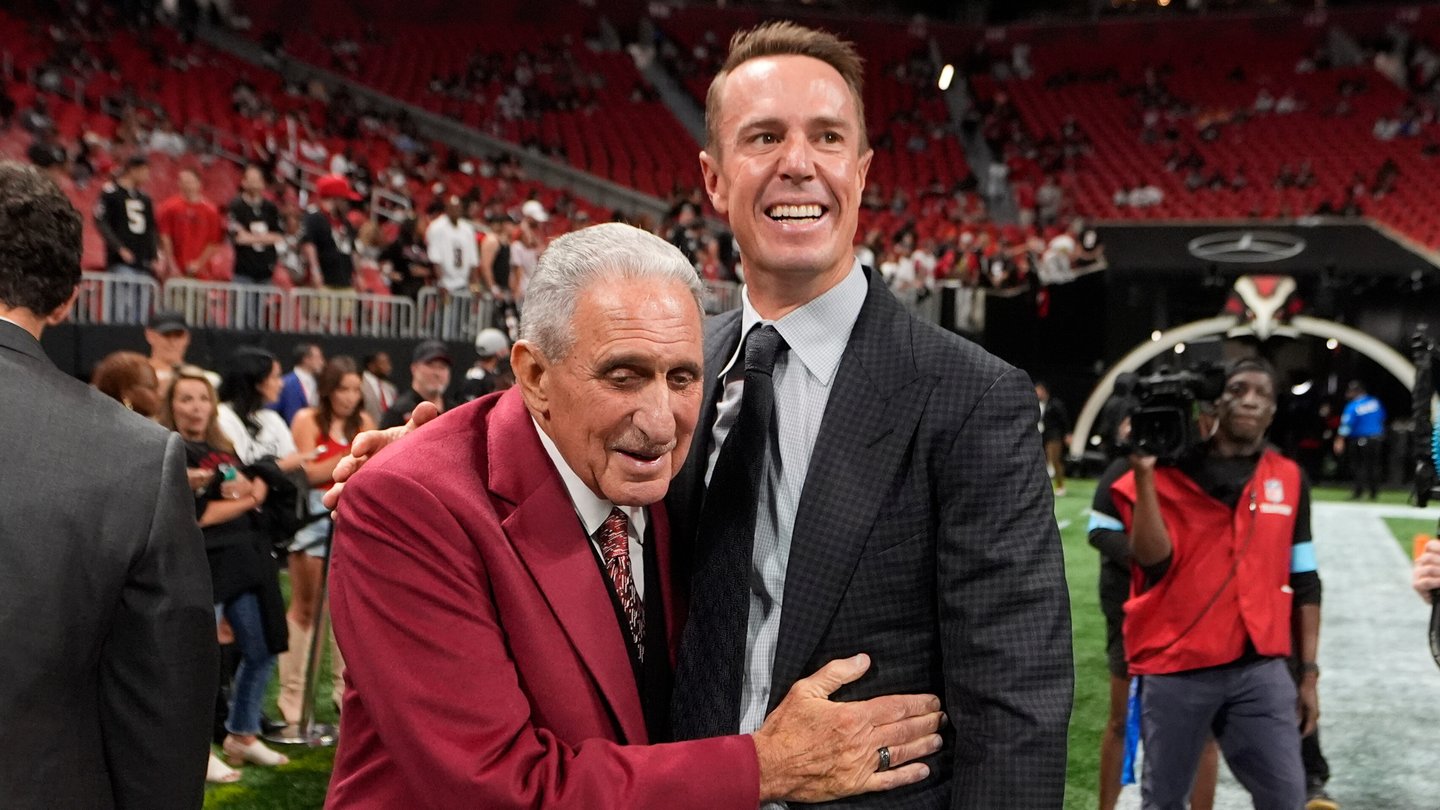 Arthur Blank, left, embraces Matt Ryan, right, on a football field