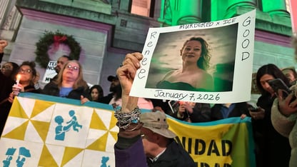 Protesters hold up signs and a photo of Renee Good in front of a building
