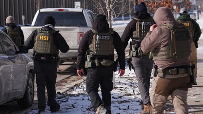 Federal immigration officers walk away on a snowy ground.