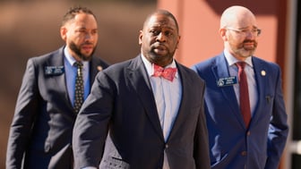 Three men in suits walk through a parking lot