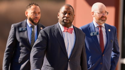 Three men in suits walk through a parking lot