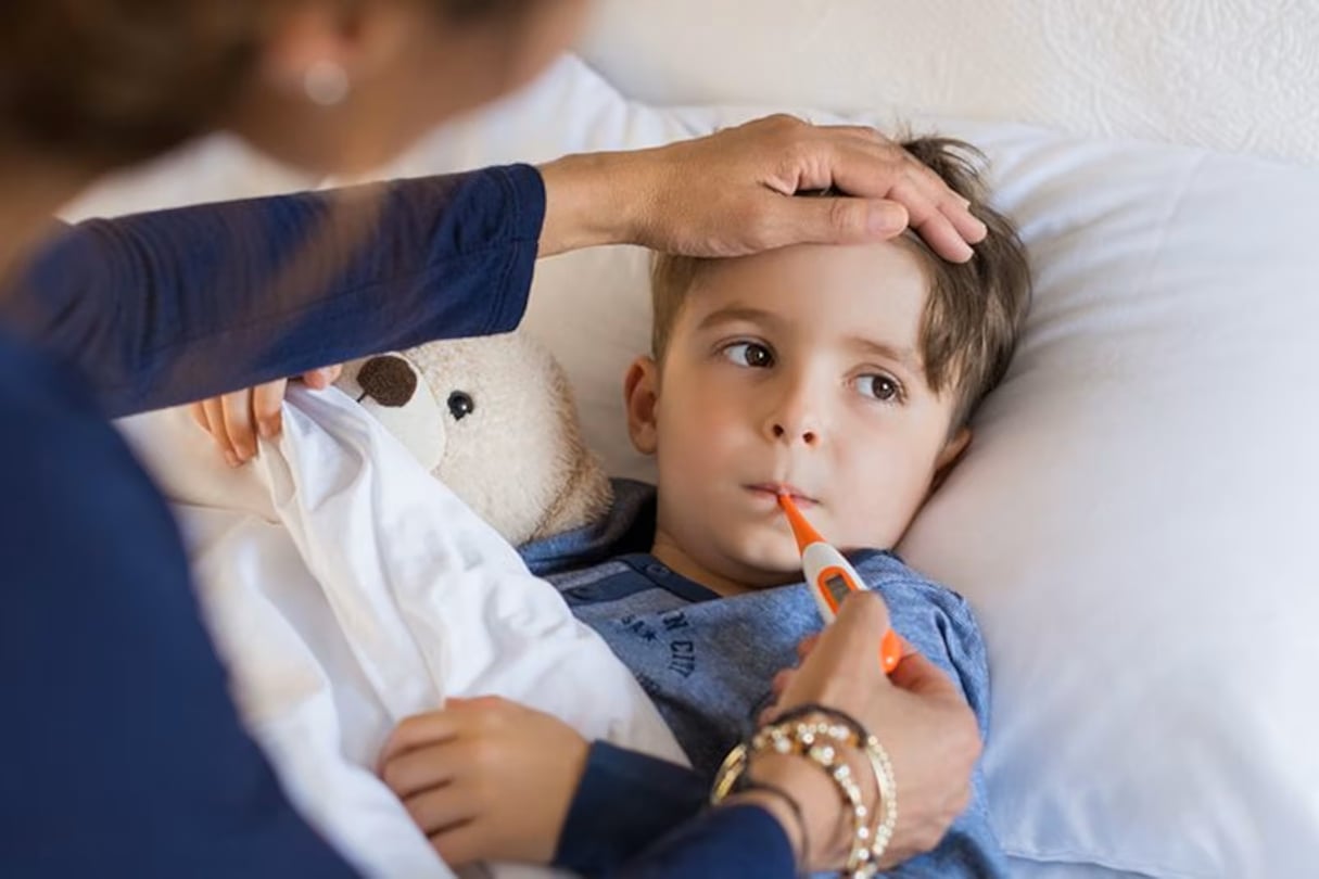 A sick child gets his temperature taken with a orange thermometer.