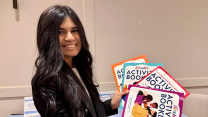 A woman holds up four activity booklets for children