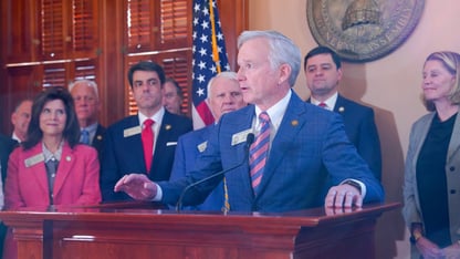 A group of lawmakers stand behind a podium for a press conference.