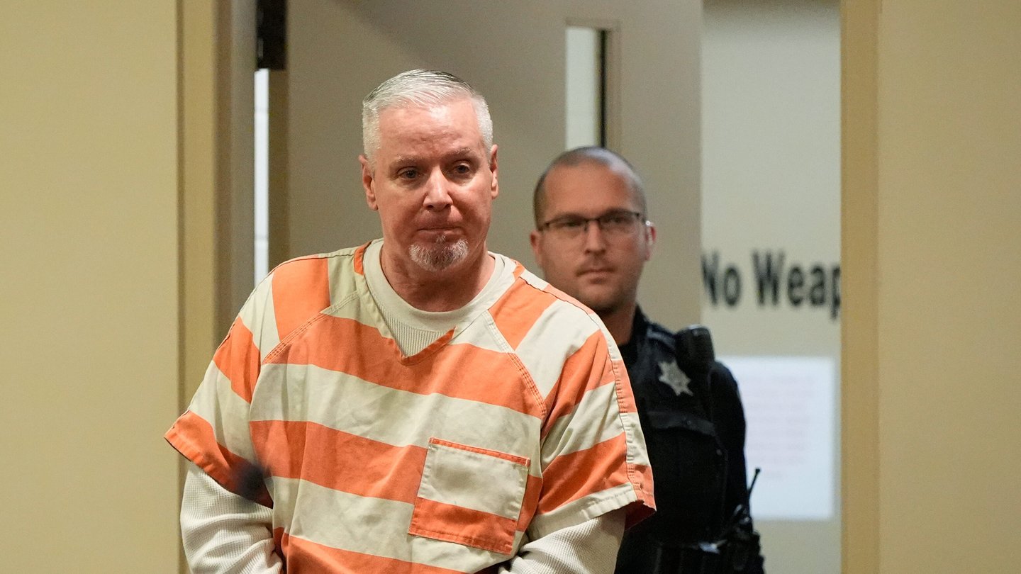 Colin Gray handcuffed in a orange and gray prison uniform.