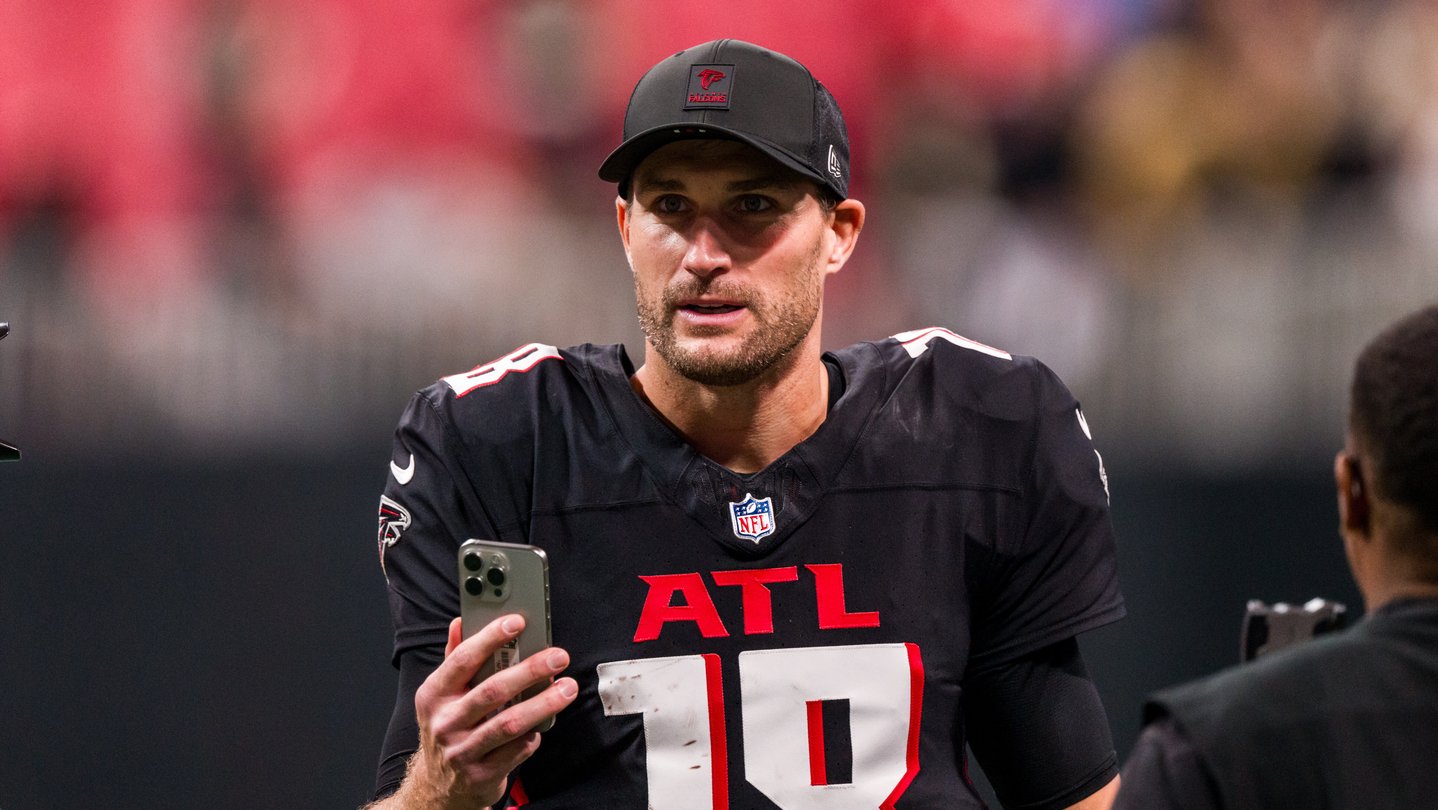 Quarterback Kirk Cousins wears a baseball cap and holds a phone