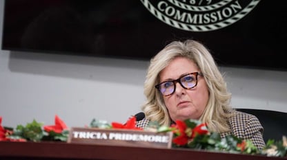 A woman wearing glasses sits behind a desk