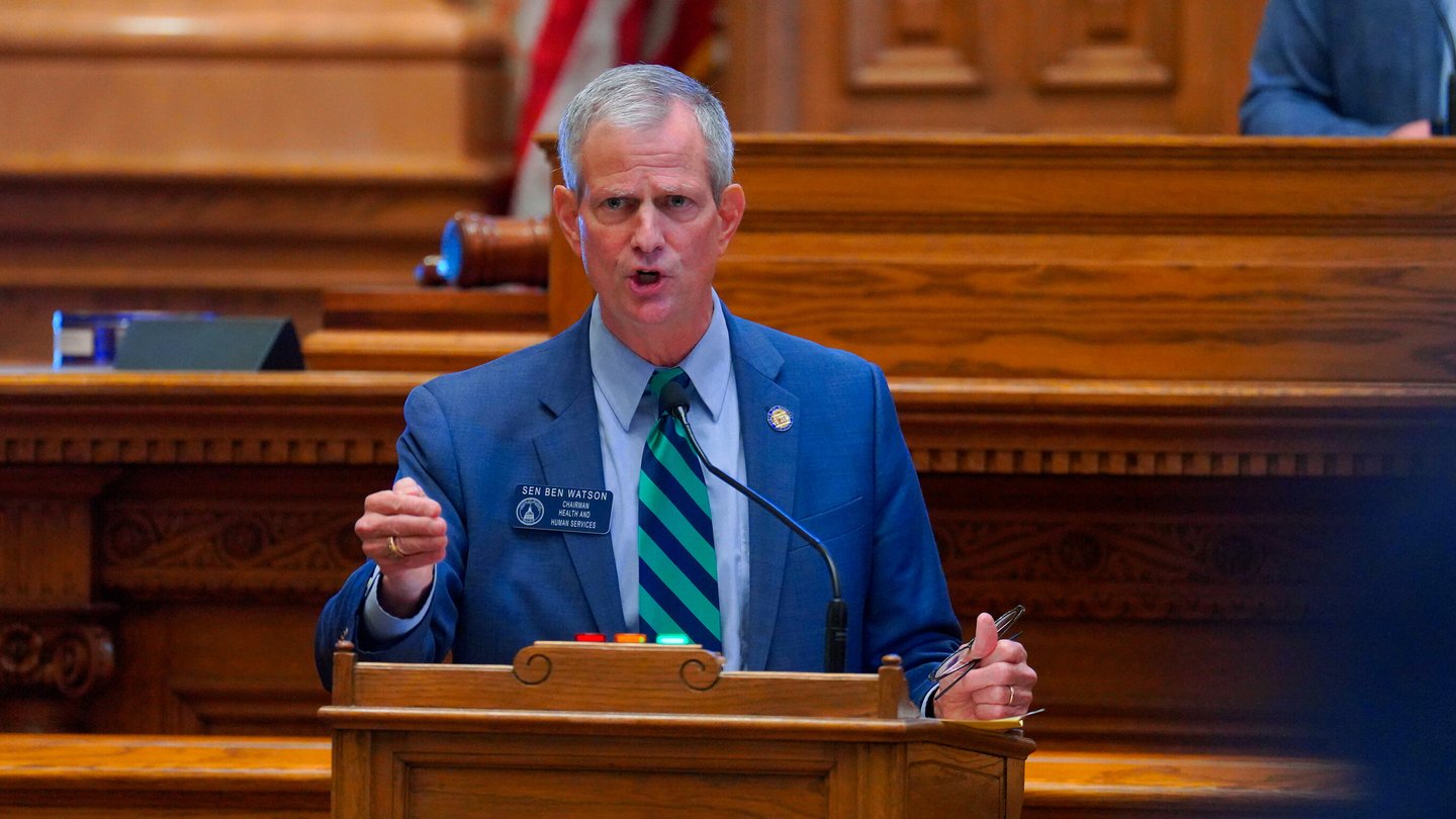 A lawmaker wearing a blue suit stands at a podium in the Georgia Senate chamber