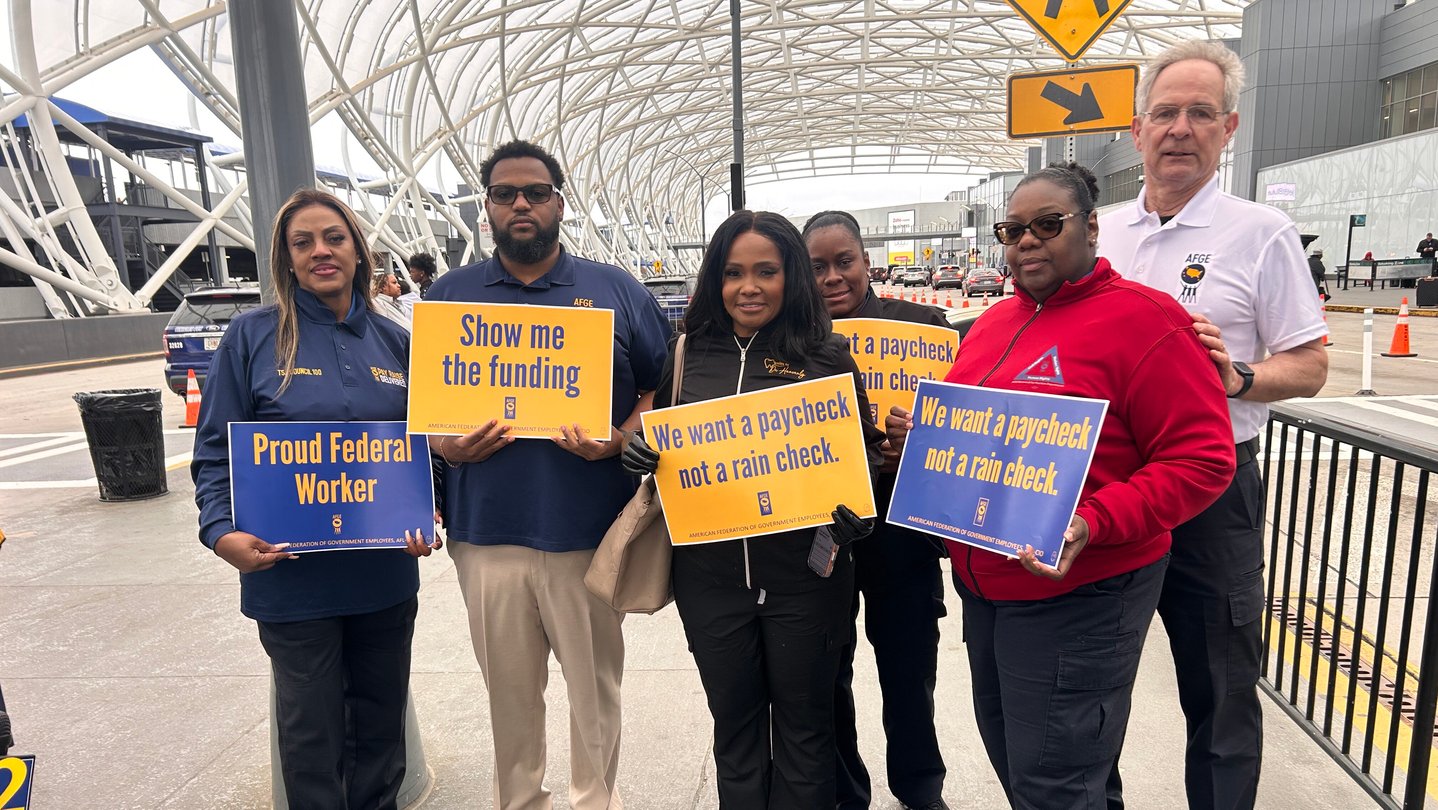 Several people stand outside an airport terminal carrying blue and yellow signs