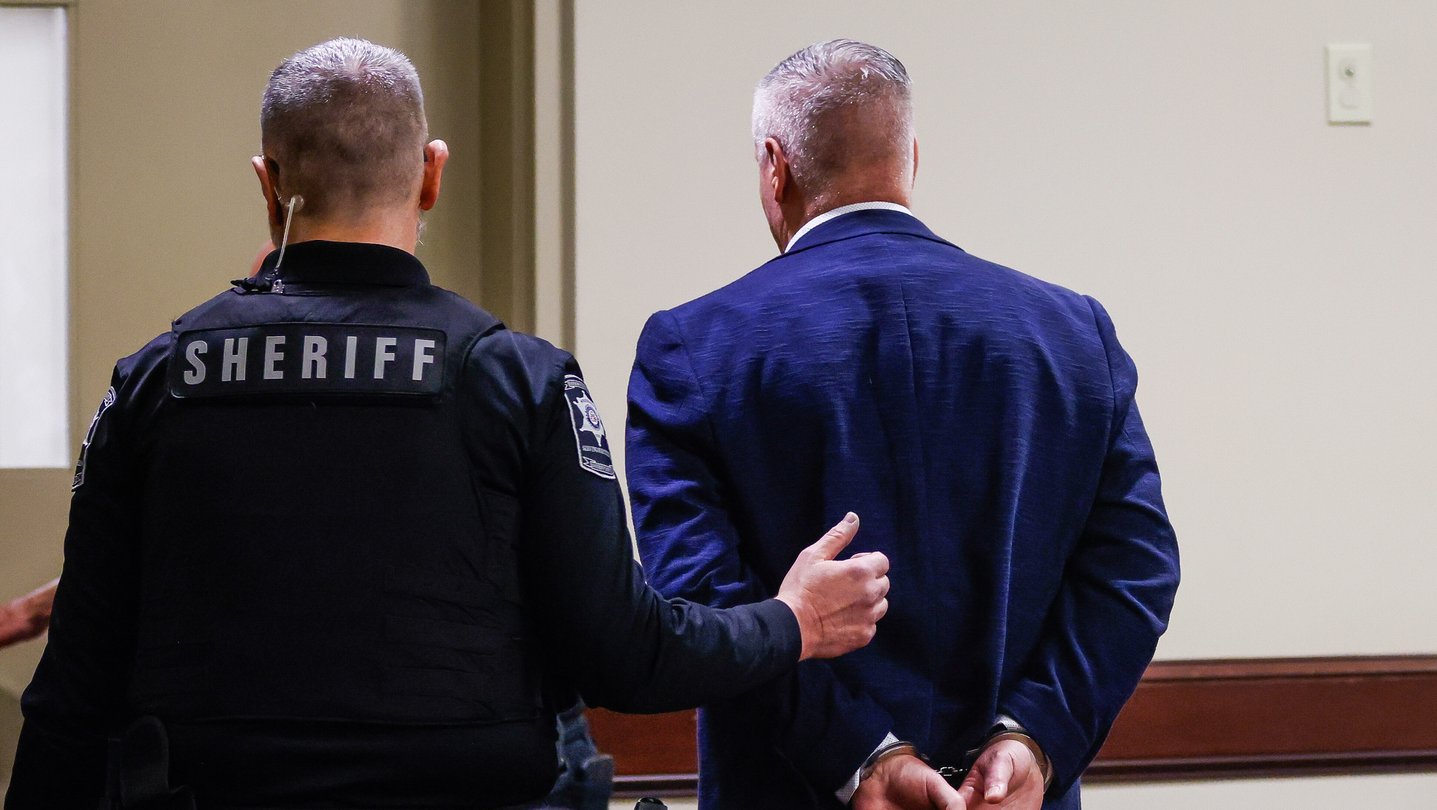 Colin Gray is handcuffed and escorted out of a room