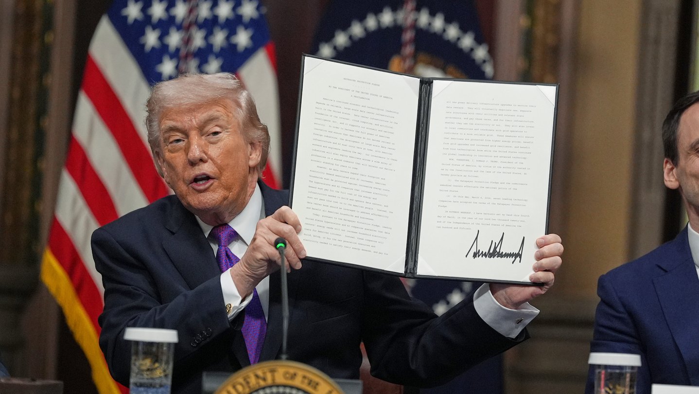President Donald Trump holds up a document while sitting at a desk