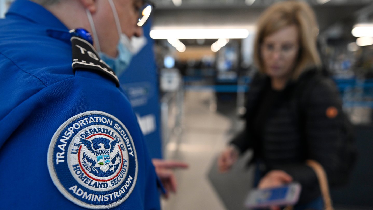 A TSA agent with a badge on his blue uniform checks a passengers ticket