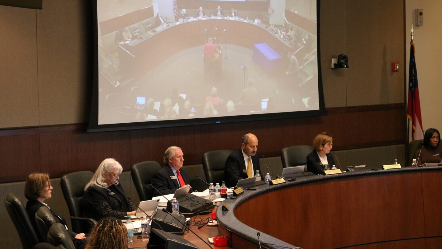 Several people sit at a board meeting in front of a projection.