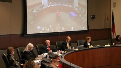 Several people sit at a board meeting in front of a projection.