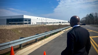 Raphael Warnock looks at a large warehouse while standing on a road