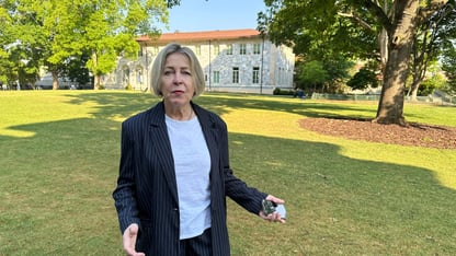 A woman stands and speaks on the lawn of the Emory University campus. A white building is in the background.