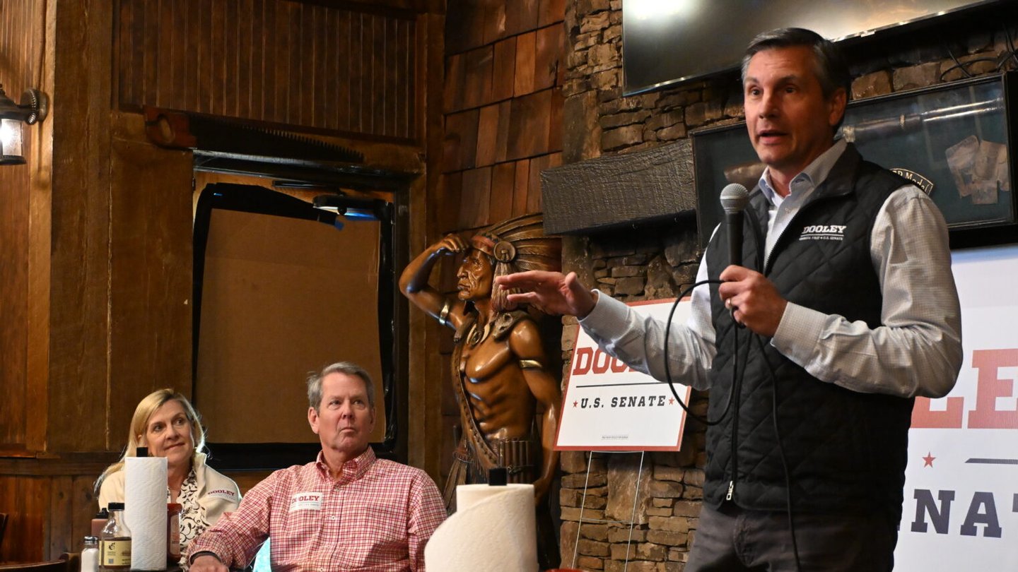 Derek Dooley stands with a microphone in his hand while the governor and his wife sit next to him.