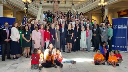 A large group of people stand on a wide set of white stairs. Several children sit on the ground in front.