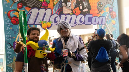 Several people wearing cosplay stand under a sign that says Momocon