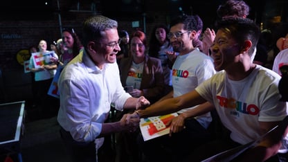 A man in a button-down shirt shakes hands with people in a large crowd