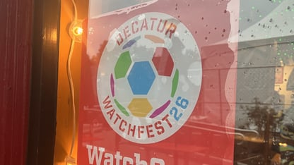 A red sign with a color soccer ball on it advertising Decatur WatchFest26