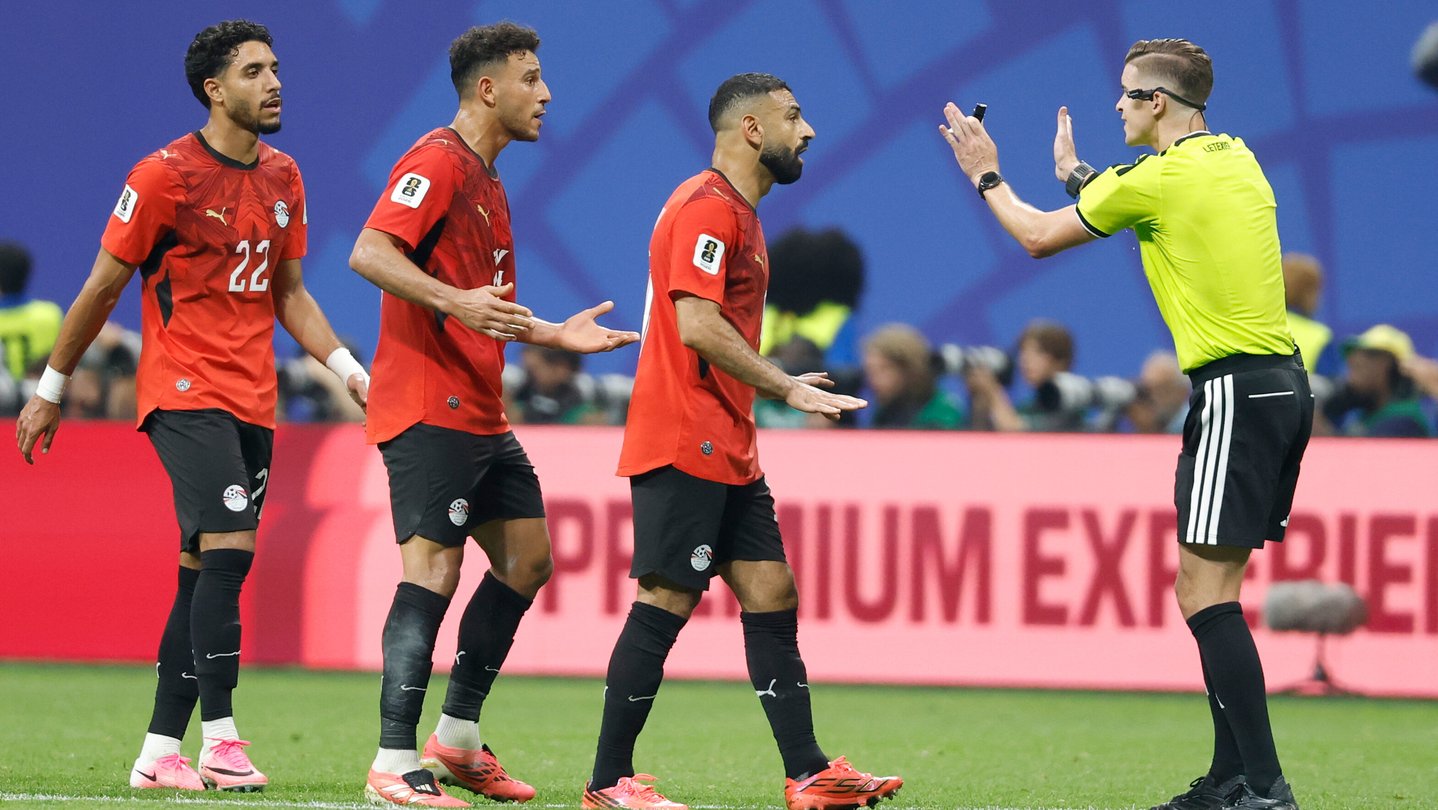 Three Egyptian players in red jerseys face a referee in a bright yellow jersey.