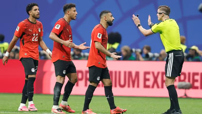 Three Egyptian players in red jerseys face a referee in a bright yellow jersey.